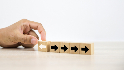A hand moving a wooden block with a left-pointing arrow away from a row of blocks pointing right