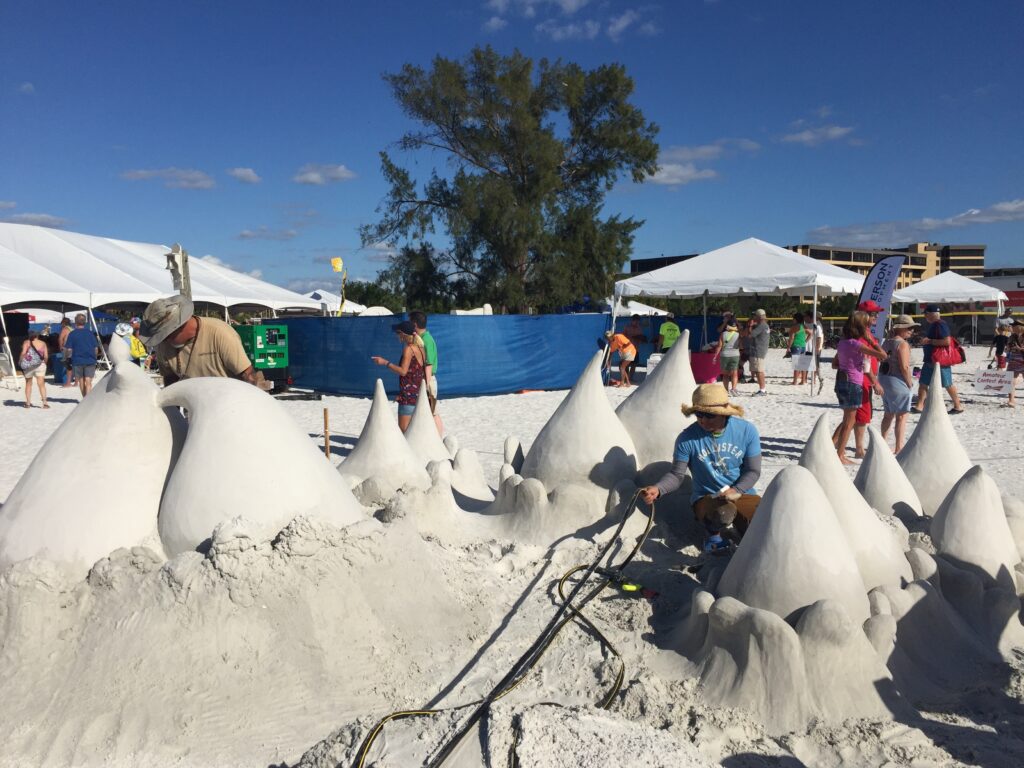 Sand sculptors shaping large wave-like formations at a beach sand-sculpting festival
