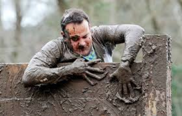 Muddy runner climbing over an obstacle during an obstacle-course race