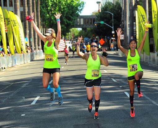 Three runners celebrating with raised arms as they approach the finish line