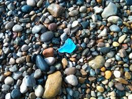 Piece of blue sea glass among rocks and pebbles on a beach