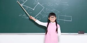 Young girl in glasses pointing at a diagram on a chalkboard, role-playing as teacher